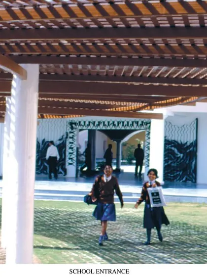 A historic photograph from 1996 shows the entrance of Babrala School. The shaded pergola and open lawn create a welcoming transition into the learning environment, a design principle we have carried through our work for decades.