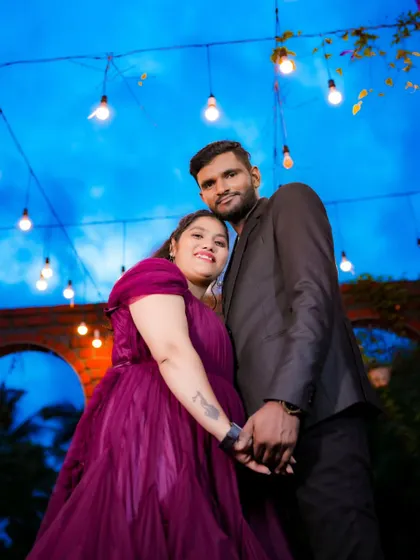 A beautiful low-angle shot of a couple under a canopy of hanging lights. The blue hour sky adds a magical touch to this pre-wedding photo.