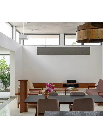 The double-height living and dining area in the SAMAM House, demonstrating our use of volume to create a sense of spaciousness. Large windows frame views of an outdoor courtyard and a tranquil Buddha statue, integrating calm and nature into the main living space.