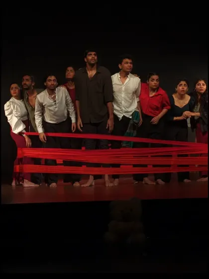 A tense and powerful tableau from 'Sea's Fire', where performers use a red cloth to symbolize connection and struggle.