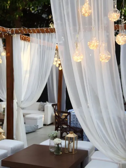 A serene outdoor lounge area with sheer white canopies and soft lighting. This setup creates a peaceful and elegant retreat for guests to relax and socialize during an evening celebration.