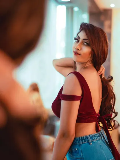 Model in a red velvet crop top and jeans, looking over her shoulder towards the camera