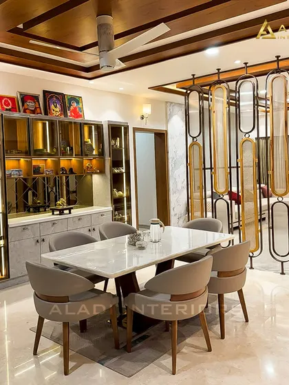 A luxurious dining room setup with a view of the living area through an elegant metal and fabric partition. The lit crockery cabinet and wooden ceiling add warmth and grandeur.