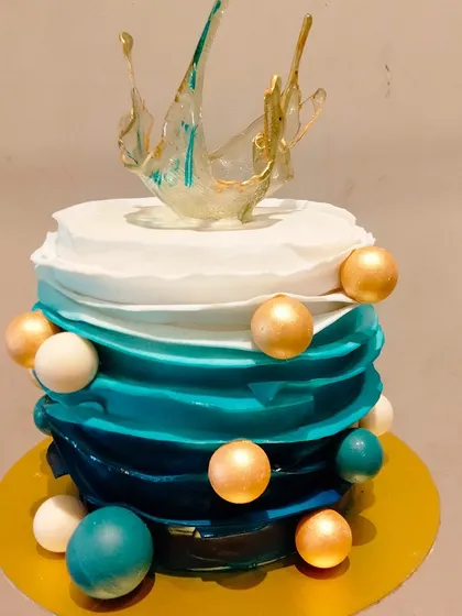 A beautiful ombre cake in shades of blue and white. The cake is decorated with different sized spheres and a delicate sugar splash on top, creating a modern and artistic look.