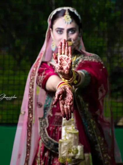 A creative bridal pose, with the bride's mehndi-covered hands held forward, framing her face beautifully.