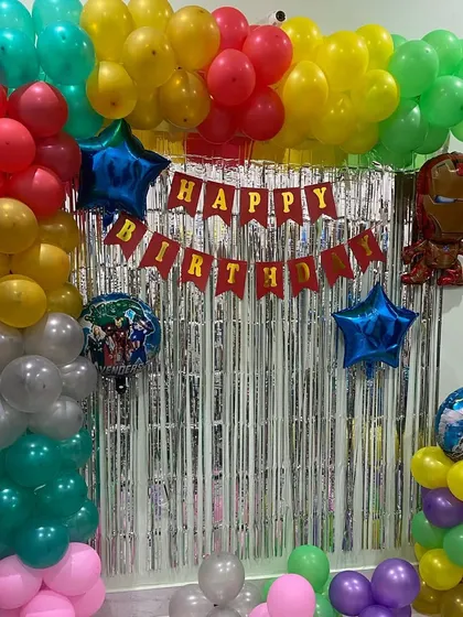 An action-packed Avengers theme birthday party. This simple home setup includes a balloon arch with character foil balloons like Iron Man, set against a silver foil curtain.