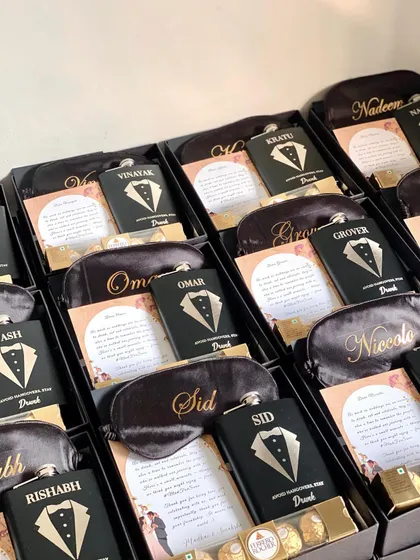 A full view of the customized groomsmen hampers, each with a personalized eye mask and hip flask. The black and gold theme is always a classic and sophisticated choice.