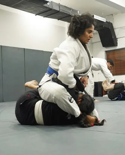 A female student in a white Gi practices maintaining the mount position. We emphasize live drilling to ensure our students can apply what they learn.