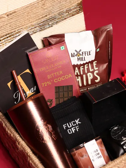 A close-up of the contents of the men's Christmas hamper, highlighting the rich cocoa, waffle chips, and cheeky "Fuck Off" socks.