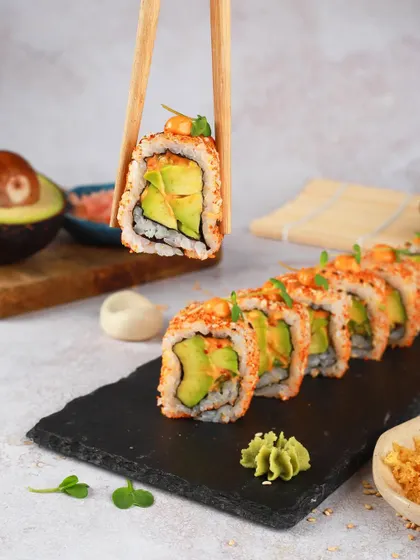 A classic avocado sushi roll, with one piece held up by chopsticks to show the fresh ingredients inside.