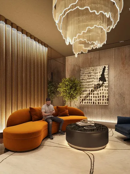 The lounge area in the Palais Royale lobby, designed to craft a lifestyle of understated grandeur. A bespoke chandelier hangs over a curved orange sofa, creating an intimate seating arrangement within a grand, opulent space.