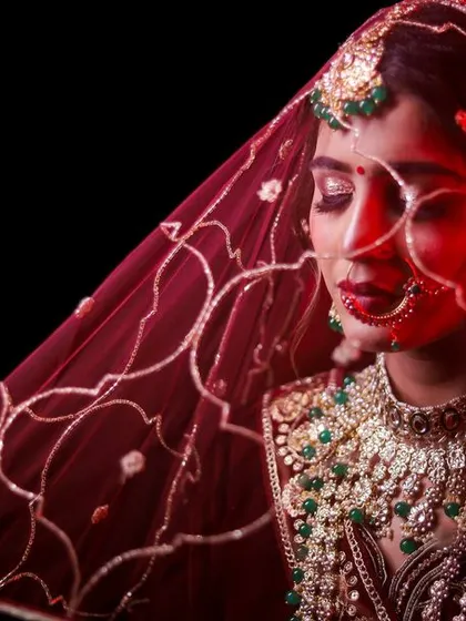 A creative bridal portrait using a red veil to create a powerful, artistic effect. The bold color and soft light emphasize the bride's features and the richness of her traditional wedding attire.
