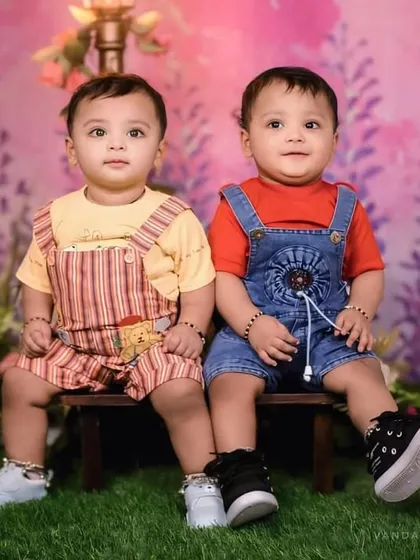 A delightful studio portrait of two young siblings for Raksha Bandhan. Dressed in adorable overalls, they sit side-by-side, showcasing their cute and innocent bond.