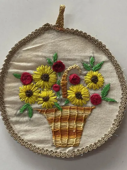 A lovely hand-embroidered basket of sunflowers and roses. This piece demonstrates various stitches, including satin stitch and woven wheel stitch, to create texture and depth.