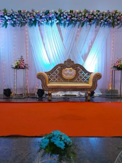A centered view of the reception stage from a distance, showing the full effect of the lighting and floral decor. The orange aisle provides a vibrant contrast to the cool tones of the stage.