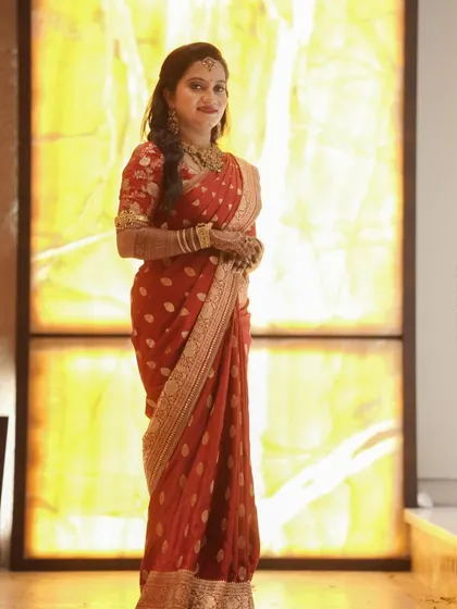 This client looks stunning against a warm, glowing backdrop. Her red saree and custom-designed blouse create a timeless and sophisticated look for the occasion.