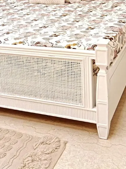 A detailed shot of the footboard on our white cane bed. You can see the combination of the woven cane panel and the classic turned-wood post, details that define its quality craftsmanship.