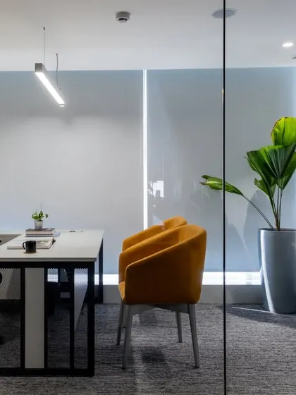 A private cabin within the open office, enclosed by glass to maintain visual connectivity. The pop of color from the visitor's chair adds personality to the professional setting.