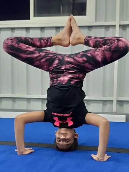 A student holds a perfect tripod headstand with a straddle, showing incredible balance and core control.