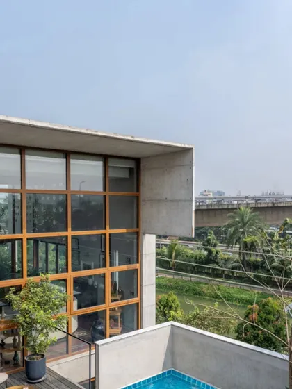 An exterior view of the 10,000 sq. ft. Dhaka residence, showcasing its bold, contemporary architecture. The combination of concrete, wood, and vast glass panels creates a structure that is both modern and connected to its lush, green surroundings.
