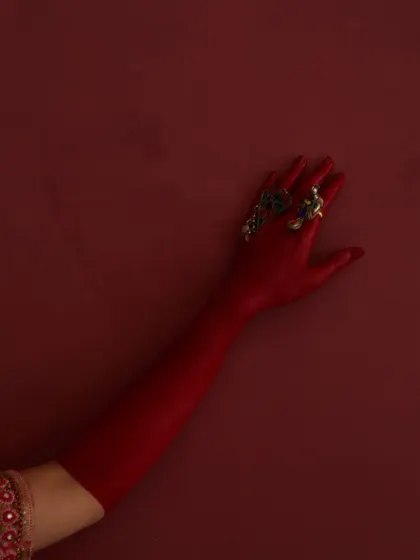 A highly conceptual and artistic shot. The focus on the arm painted red, adorned with traditional rings, creates a powerful visual against a solid red background. It’s a detail shot that is both abstract and culturally rich.