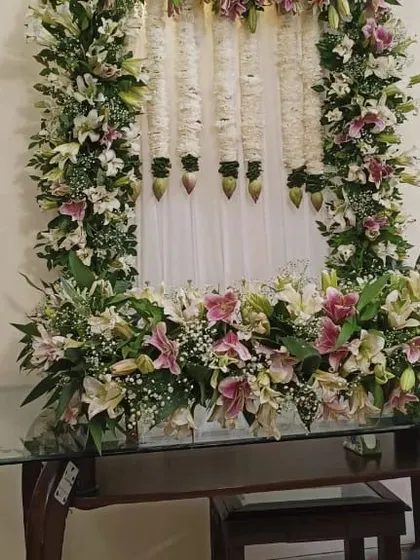 Another angle of the elegant lily flower decor for a Ganpati puja, showing the full floral frame on a glass table.