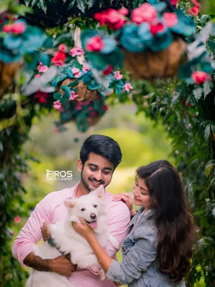 A lovely portrait of a couple and their white dog framed by a floral archway. The genuine smiles and the way they hold their pet show the love they share as a small family.