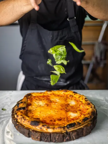 A dynamic shot of fresh basil leaves being tossed onto a finished pizza. It captures the energy of the kitchen and the freshness of my ingredients.