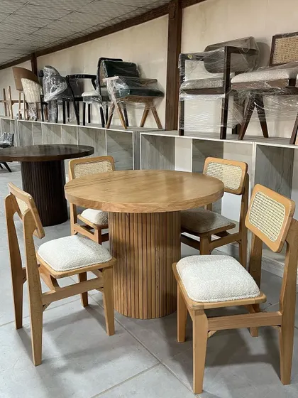 A four-seater dining set featuring a round table with a fluted wooden base and a light wood top, paired with matching cane-back chairs.
