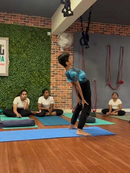 A student prepares for a standing backbend, opening his chest towards the sky. This builds strength in the legs and flexibility in the spine.