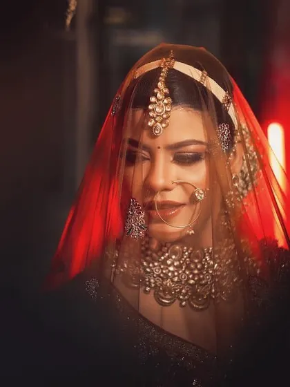 A moody and beautiful bridal portrait with the bride's face partially obscured by her red veil. The dramatic lighting creates a sense of mystery and elegance.
