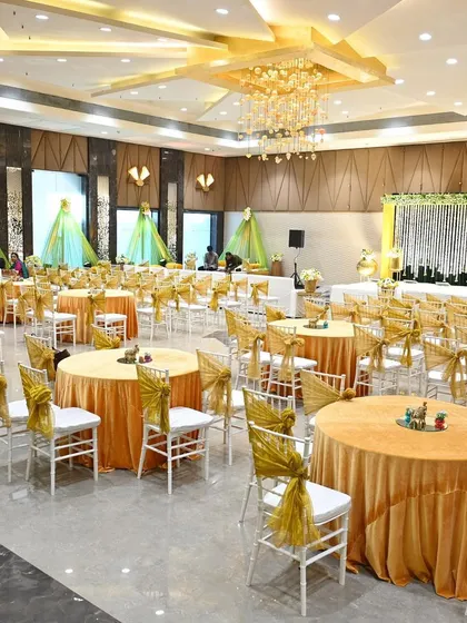 A wide view of the banquet hall set up for a Mehendi ceremony. The gold and white color scheme with pops of green creates an elegant and celebratory environment for guests.