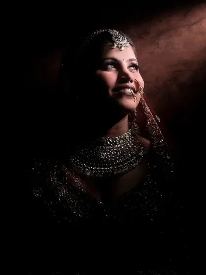A low-light portrait of a bride, her face illuminated beautifully, highlighting her smile and traditional jewelry.