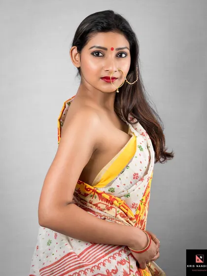 A classic portrait of a woman in a traditional Bengali saree with a large nose ring. The simple grey background and direct gaze create a powerful and expressive image focused on cultural beauty.