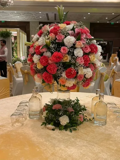 A lush and colorful floral centerpiece for a guest table. This large arrangement of pink, peach, and white roses adds a touch of luxury and beauty to the dining experience.
