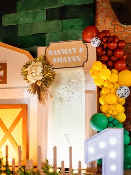 A close-up of the personalized sign for Sanmay and Smayan's party, accented with a wheat sheaf and a colorful balloon garland.
