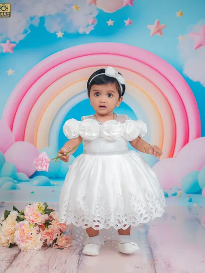A dreamy first birthday setup with a pastel rainbow and clouds. This little angel looks perfect in her white dress.