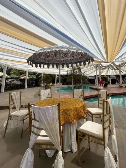 Poolside seating arrangement for a relaxed Mehendi or Haldi event. The decor includes elegant table settings with traditional Indian-print umbrellas.