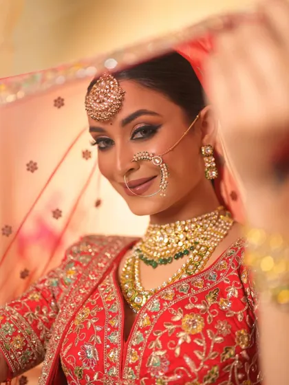 A classic bridal portrait. The focus here is on the sharp, defined eyes and flawless base, complemented by a traditional red lehenga and gold jewellery, embodying timeless bridal beauty.