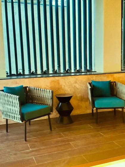 Elegant outdoor armchairs on a Jaipur balcony. The combination of woven material and teal cushions adds texture and a pop of color to the space.
