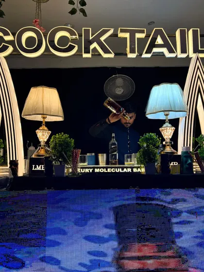 A bartender meticulously pours a drink at a beautifully symmetrical 'COCKTAIL' station, demonstrating precision and focus.