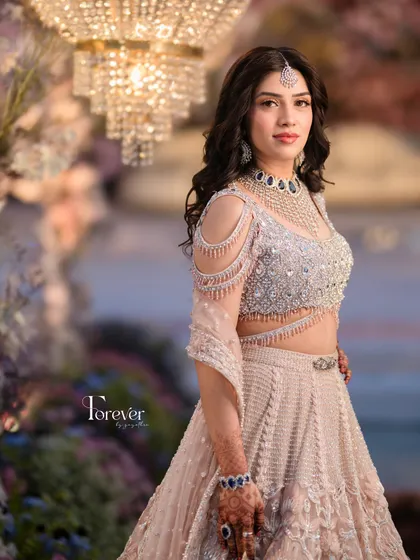 A close-up of the bride, showcasing her intricate jewelry and the beautiful ambient lighting of the reception decor. The warm glow from the chandeliers adds a soft, romantic feel to the portrait.