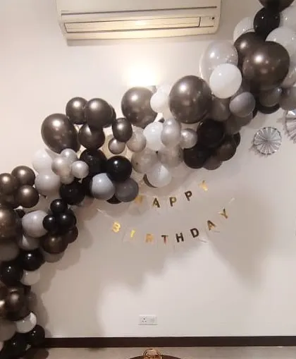 A modern and stylish home birthday decoration. A balloon garland in black, white, and chrome elegantly drapes across the wall.