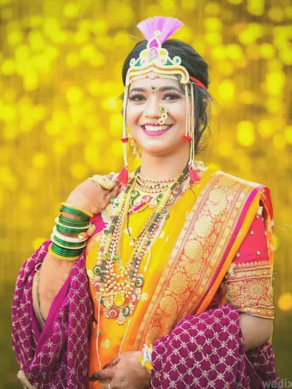 A classic portrait of a Maharashtrian bride in a yellow Paithani saree, adorned with traditional mundavalya and nath.