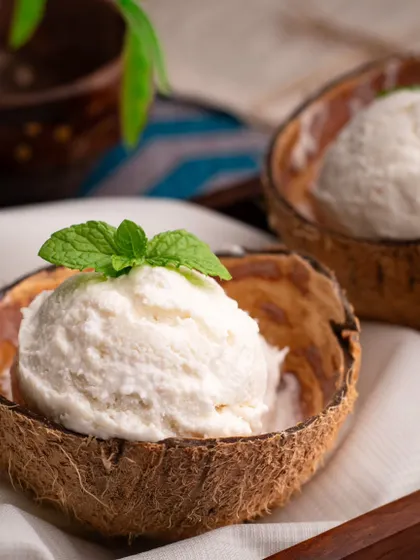 Natural and refreshing tender coconut ice cream served in a real coconut shell. The styling is simple and rustic, emphasizing the natural ingredients and tropical flavor.