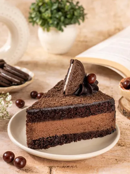 A slice of rich chocolate Oreo mousse cake, styled with a book and cherries for a cozy, indulgent feel.
