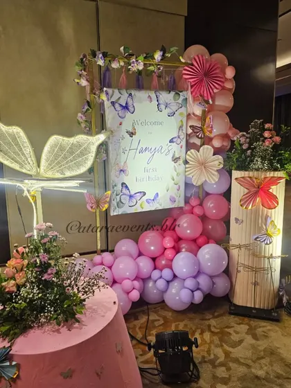 The welcome setup for Hanya's butterfly-themed first birthday. It features a beautiful sign, a cascade of pink and purple balloons, and a stunning light-up butterfly wing, setting a magical tone from the very beginning.