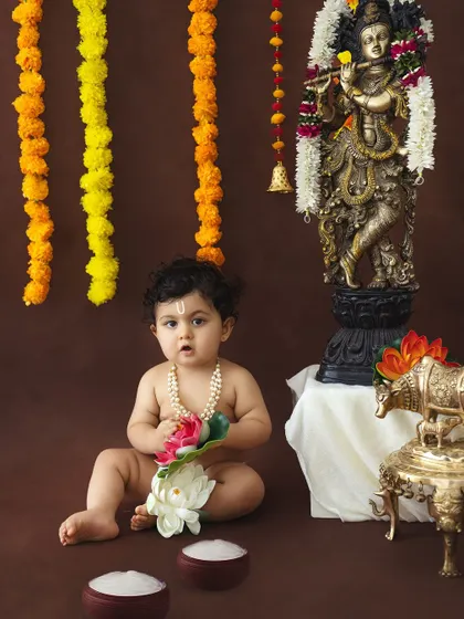 A beautiful portrait of a baby boy dressed as Krishna, holding a lotus flower.
