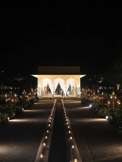 A symmetrical view of the candle-lit walkway leading to an illuminated pavilion, creating a grand and dramatic entrance for the sangeet.