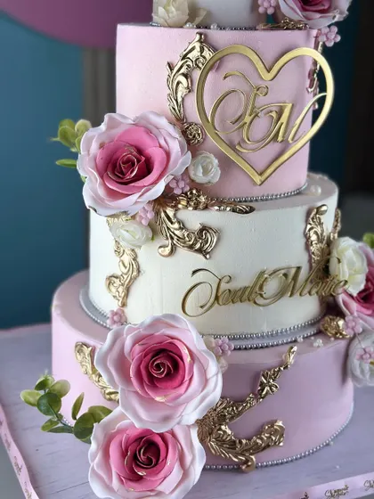 A love story in every layer. This white and pink tiered cake is a classic, featuring delicate gold accents, personalized monograms, and beautiful pink sugar roses for a truly romantic celebration.